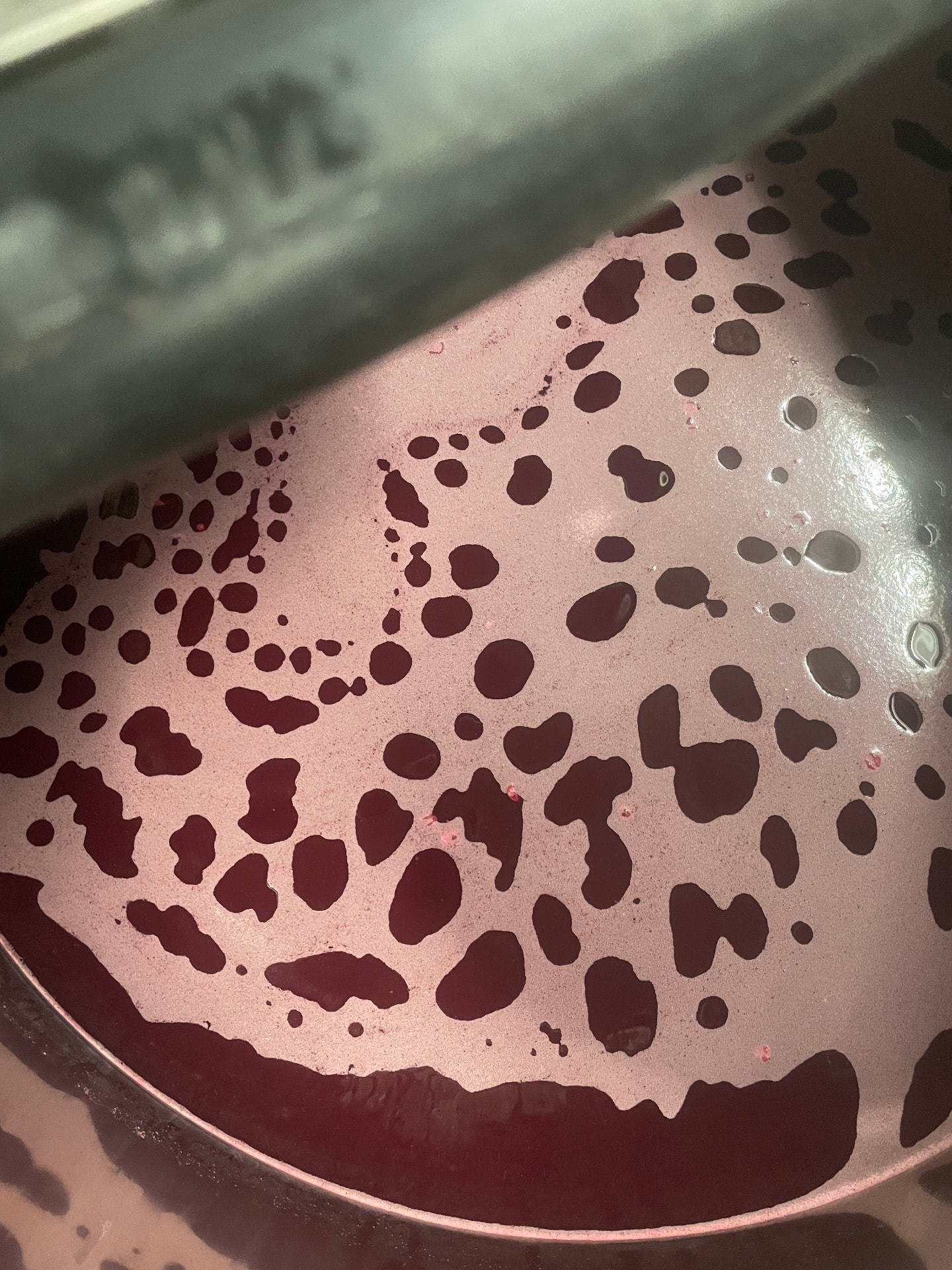 Vue plongeante dans une cuve : le moût en fermentation perce la couche de lies rosées en un réseau de cellules