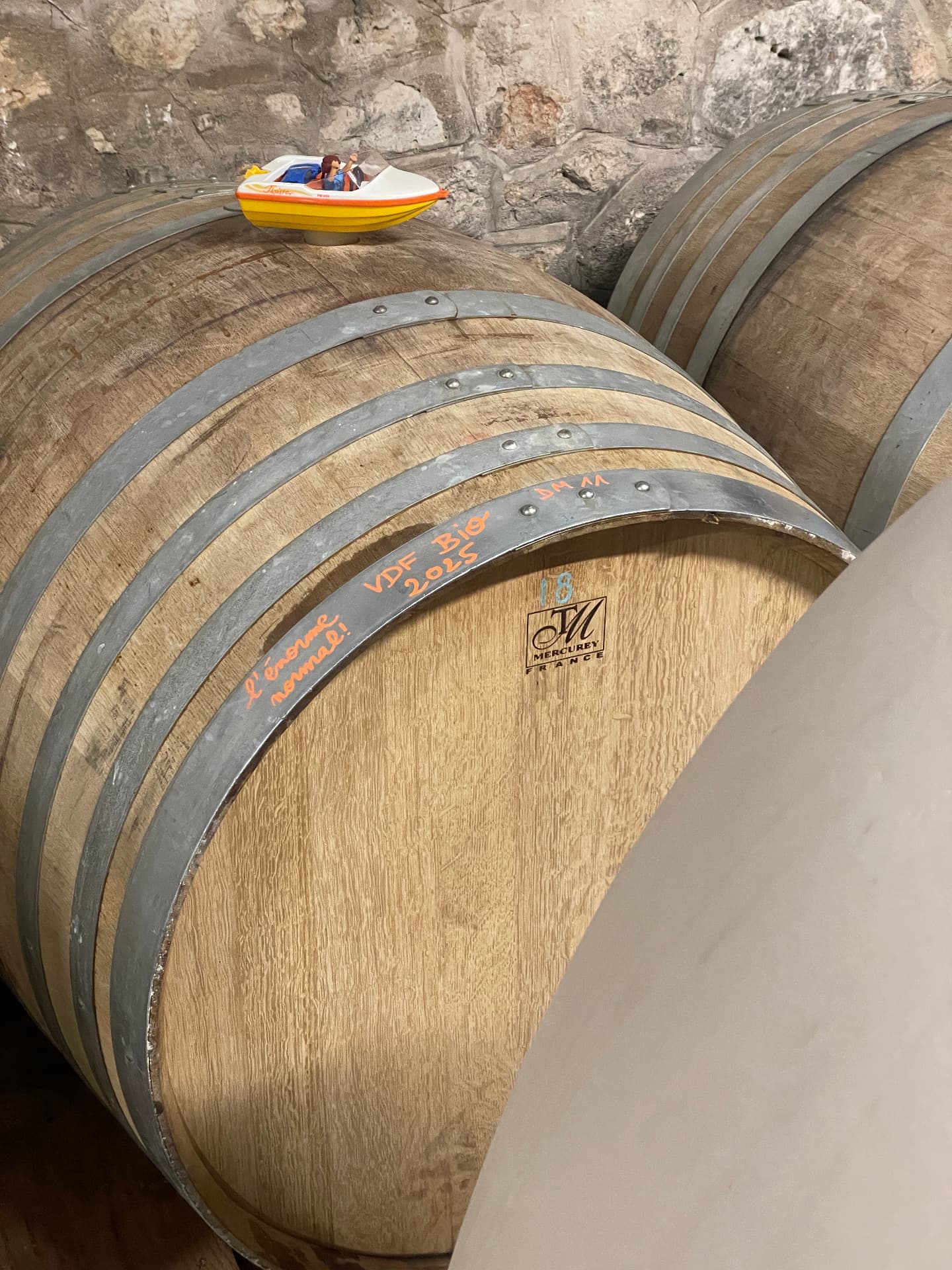 Fût de chêne marqué à la craie « VDF Bio 2025 » pour la cuvée « L’Énorme Normal », un petit bateau-jouet posé sur le dessus